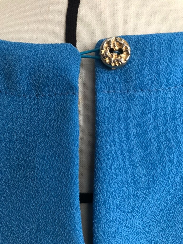 Fermeture dos en forme de goutte agrémentée d’un bouton doré